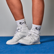 Cheerleader standing on a blue mat in white Nfinity Beast mid-top cheer shoes