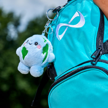 Plush globe charm keychain clipped to the side of a teal Nfinity backpack with the infinity logo.
