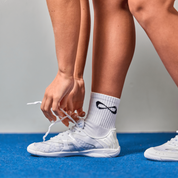 Cheerleader tying white Nfinity Vengeance cheer shoes on a blue mat